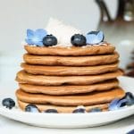 a stack of gingerbread pancakes topped with whipped cream, blueberries. and edible flowers