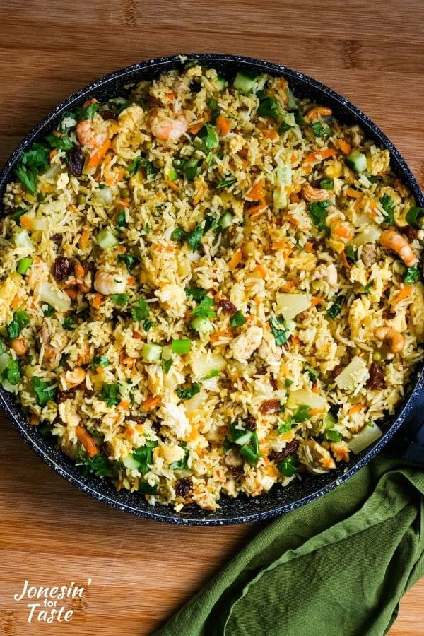 a skillet next to a green napkin on a wooden board filled with green curry fried rice