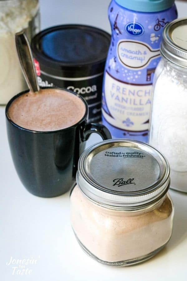 a jar of cocoa mix and a mug of hot cocoa sit next to the ingredients to make it