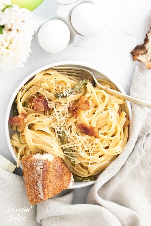 Fettucine carbonara with bacon and roasted asparagus in a white dish on white linens.