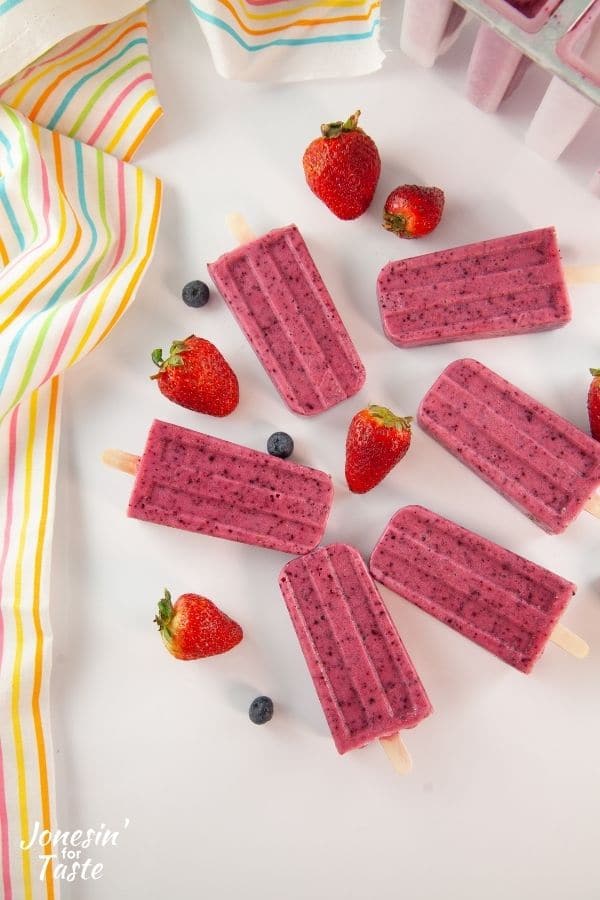 Fruit popsicles laid out on counter with strawberries and blueberries