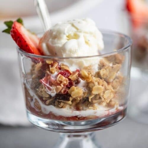 a glass bowl of strawberry rhubarb crisp with a scoop of vanilla on top