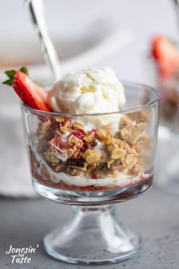 a glass bowl of strawberry rhubarb crisp with a scoop of vanilla on top